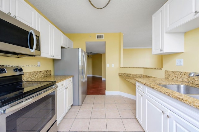 kitchen featuring light stone counters, white cabinets, sink, light tile patterned floors, and stainless steel appliances