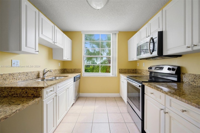 kitchen with appliances with stainless steel finishes, light tile patterned flooring, white cabinetry, a textured ceiling, and sink