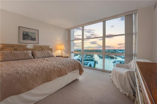 bedroom with carpet, a water view, and a wall of windows