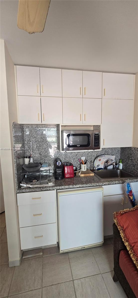 kitchen with white cabinets, light tile patterned floors, sink, dark stone counters, and decorative backsplash