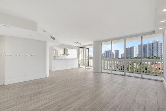 spare room featuring floor to ceiling windows, a view of city, wood finished floors, and baseboards