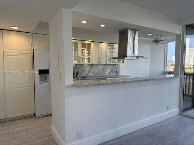 kitchen featuring white fridge with ice dispenser, white cabinets, island range hood, kitchen peninsula, and light stone countertops