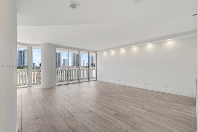 unfurnished room featuring visible vents, a city view, light wood-style flooring, a wall of windows, and baseboards