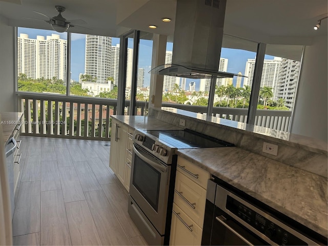 kitchen with white cabinetry, island range hood, light hardwood / wood-style flooring, stainless steel range with electric stovetop, and ceiling fan