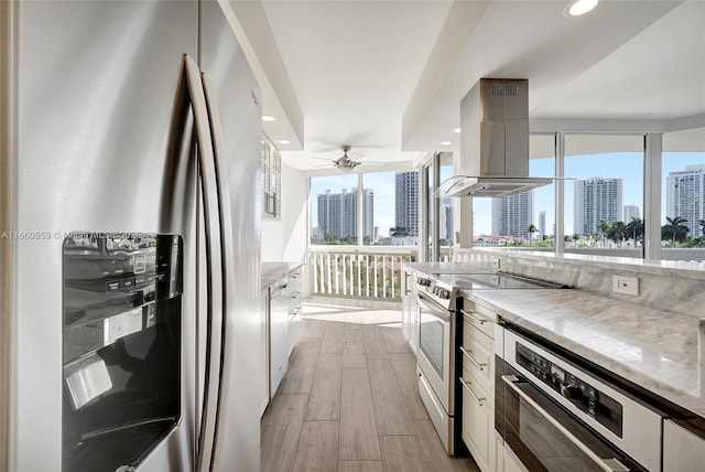 kitchen featuring light wood-style flooring, appliances with stainless steel finishes, a view of city, and island range hood