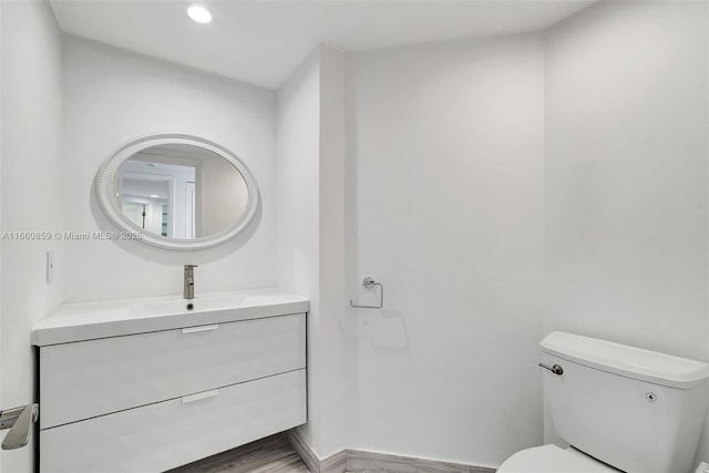 bathroom featuring baseboards, toilet, recessed lighting, wood finished floors, and vanity