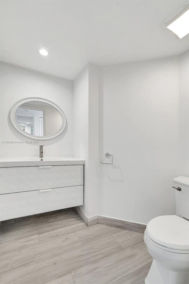 bathroom featuring baseboards, toilet, recessed lighting, wood finished floors, and vanity