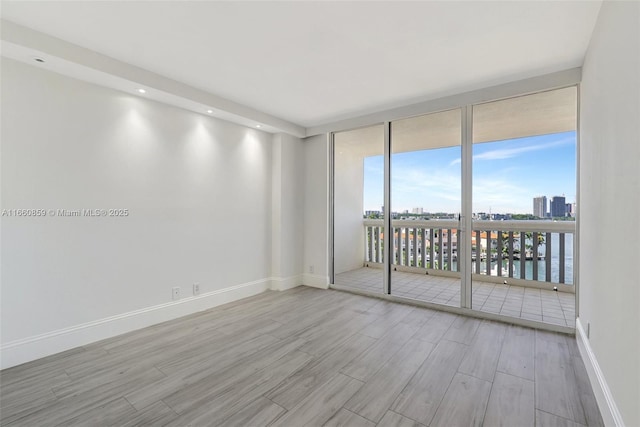 empty room with light wood finished floors, baseboards, a water view, a city view, and a wall of windows