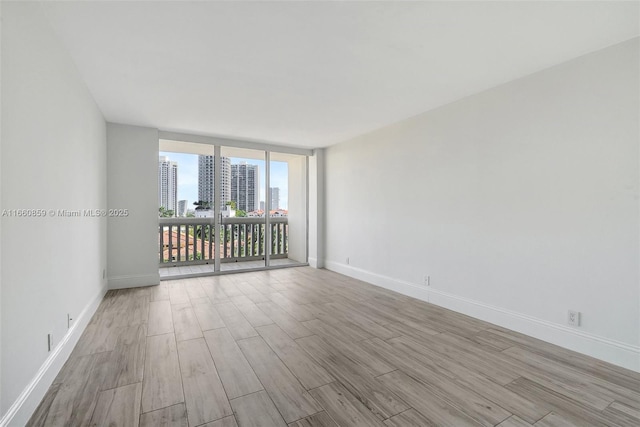 empty room with baseboards, a city view, wood finished floors, and floor to ceiling windows
