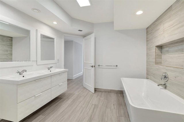 full bath featuring double vanity, recessed lighting, baseboards, and a freestanding bath