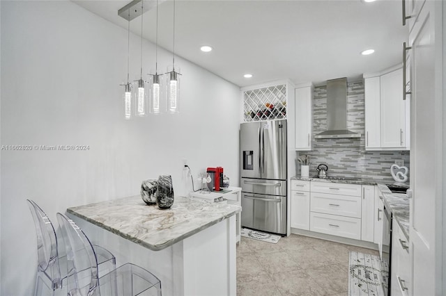 kitchen featuring light stone counters, a breakfast bar area, white cabinets, wall chimney exhaust hood, and stainless steel fridge