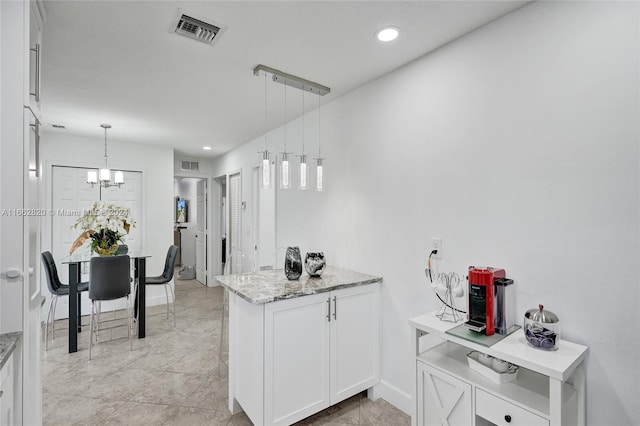 kitchen with hanging light fixtures, white cabinetry, light stone counters, kitchen peninsula, and an inviting chandelier