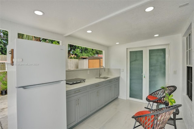 kitchen featuring gray cabinetry, white refrigerator, light tile patterned floors, a textured ceiling, and sink