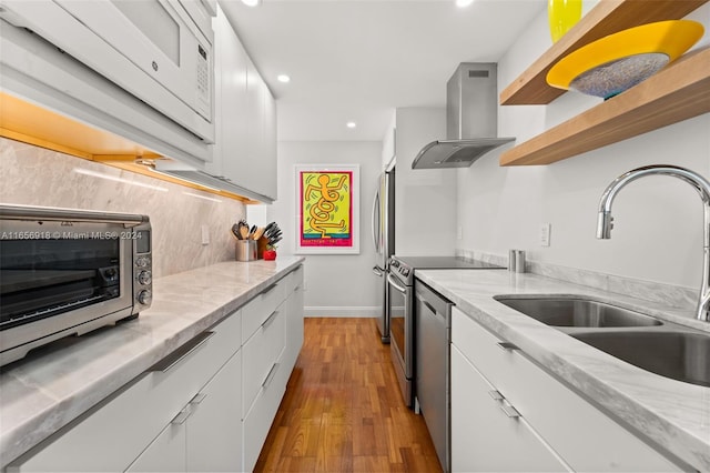 kitchen with wall chimney range hood, sink, light wood-type flooring, white cabinetry, and stainless steel appliances