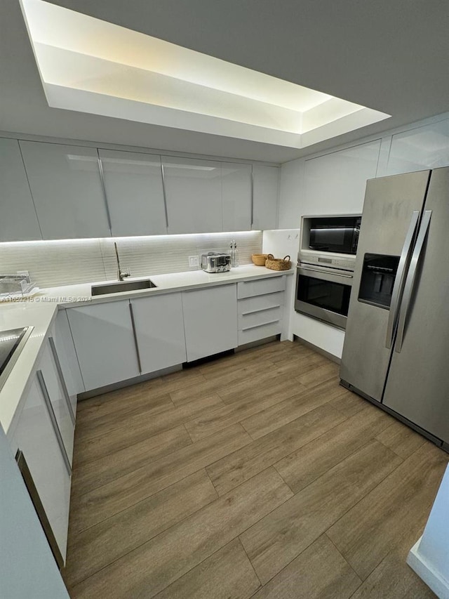 kitchen with white cabinets, stainless steel appliances, a raised ceiling, and sink