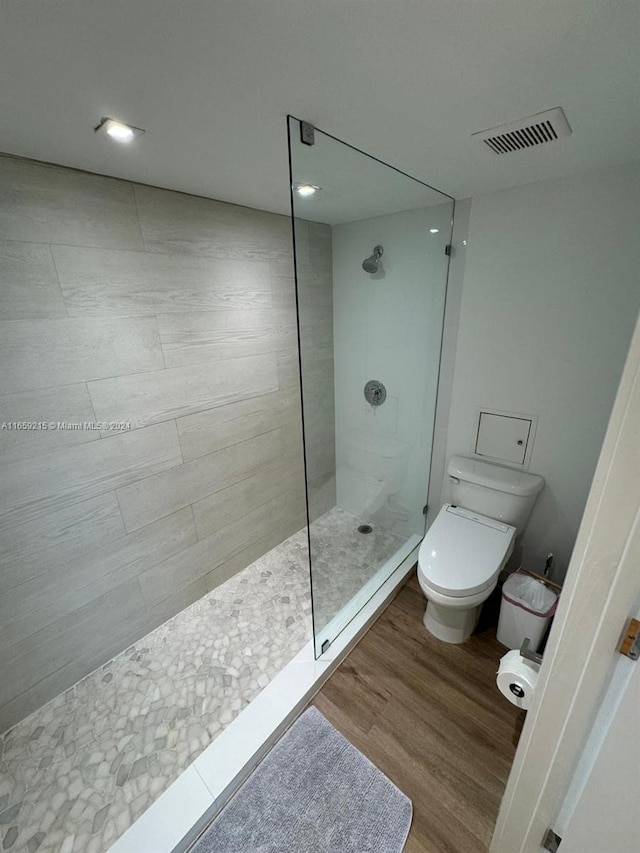 bathroom featuring wood-type flooring, toilet, and tiled shower