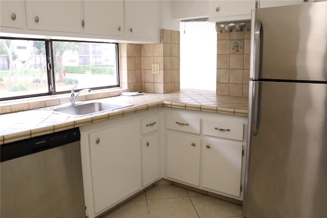 kitchen featuring appliances with stainless steel finishes, light tile patterned flooring, white cabinetry, tile counters, and sink