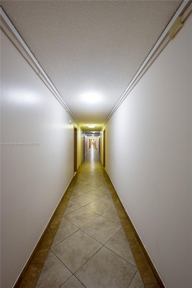 corridor featuring a textured ceiling, tile patterned flooring, and ornamental molding