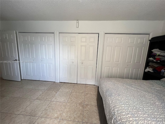 bedroom featuring multiple closets, a textured ceiling, and light tile patterned floors