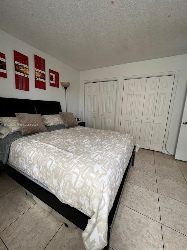 bedroom featuring a textured ceiling, light tile patterned flooring, and two closets