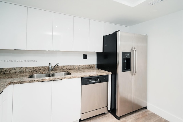 kitchen with sink, stainless steel appliances, light stone countertops, light hardwood / wood-style floors, and white cabinets