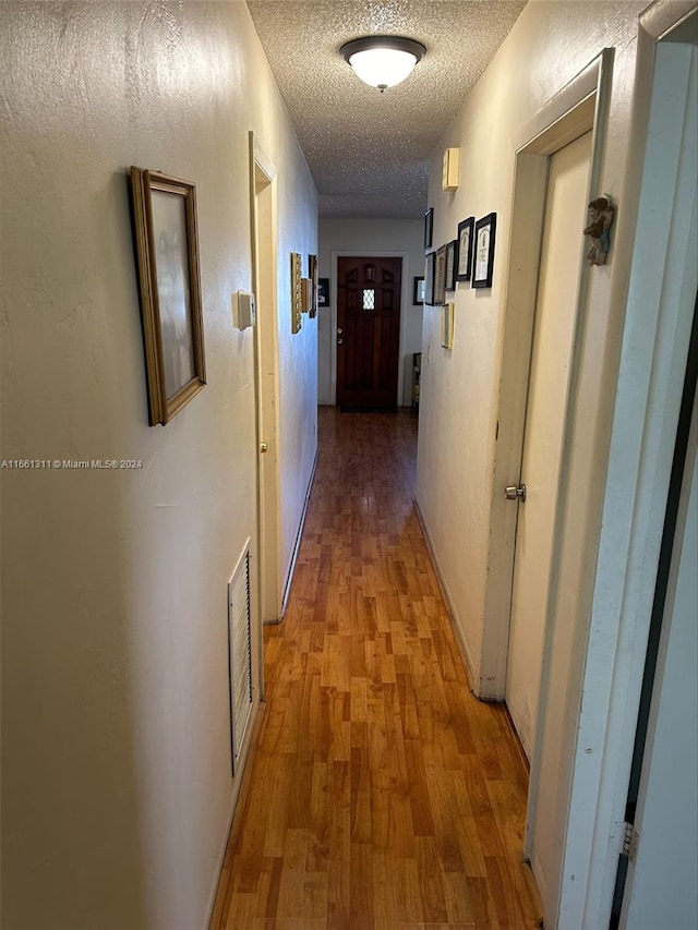 hallway with light hardwood / wood-style flooring and a textured ceiling