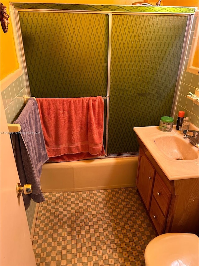 full bathroom featuring shower / bath combination with glass door, tile walls, vanity, and toilet