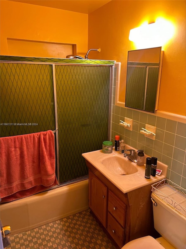 full bathroom featuring shower / bath combination with glass door, vanity, tile walls, and toilet