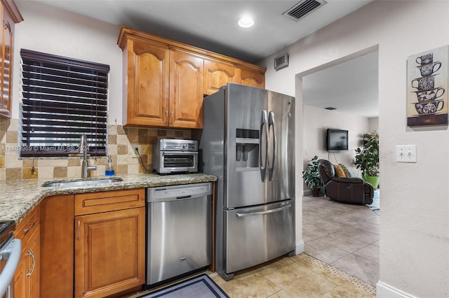 kitchen featuring light stone counters, tasteful backsplash, light tile patterned floors, stainless steel appliances, and sink