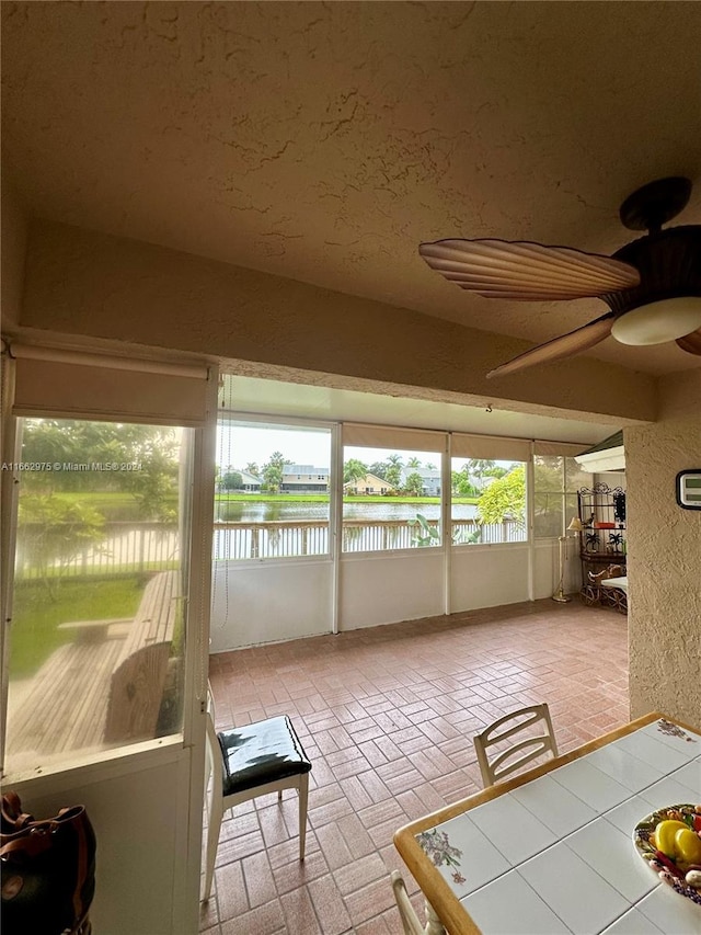 unfurnished sunroom with a water view and ceiling fan