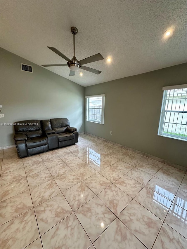 unfurnished living room with ceiling fan, a textured ceiling, lofted ceiling, and light tile patterned floors