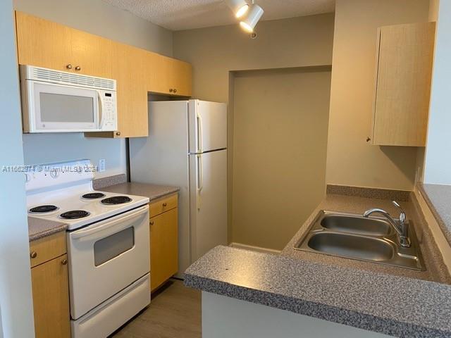 kitchen with wood-type flooring, a textured ceiling, sink, white appliances, and light brown cabinets