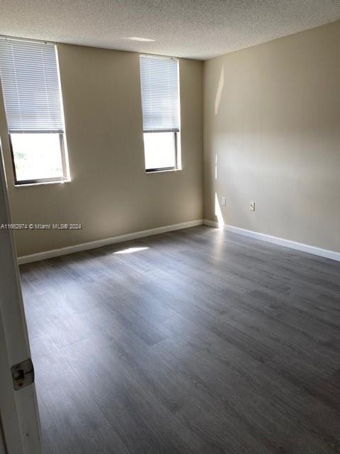 unfurnished room featuring dark wood finished floors, baseboards, and a textured ceiling