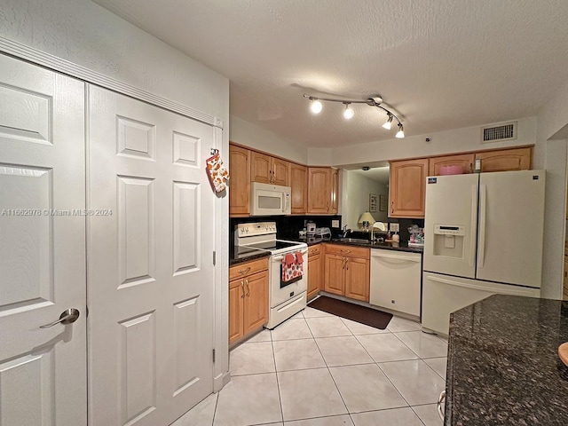 kitchen with light tile patterned flooring, white appliances, a textured ceiling, dark stone counters, and sink