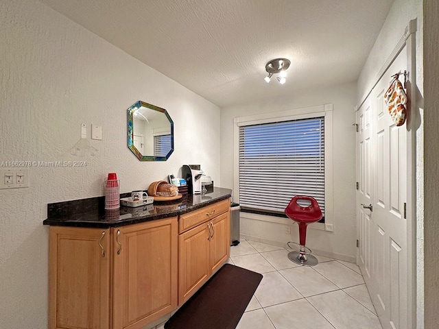 interior space with dark stone countertops, a textured ceiling, and light tile patterned floors