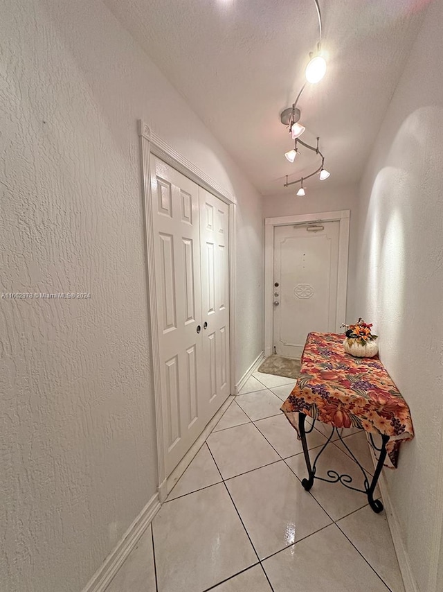 hall featuring a textured ceiling, track lighting, and light tile patterned floors