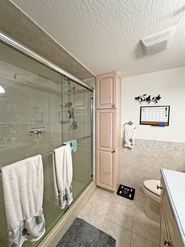 bathroom with tile walls, a textured ceiling, walk in shower, vanity, and toilet