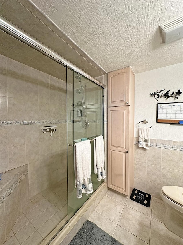 bathroom featuring a textured ceiling, tile patterned floors, walk in shower, tile walls, and toilet