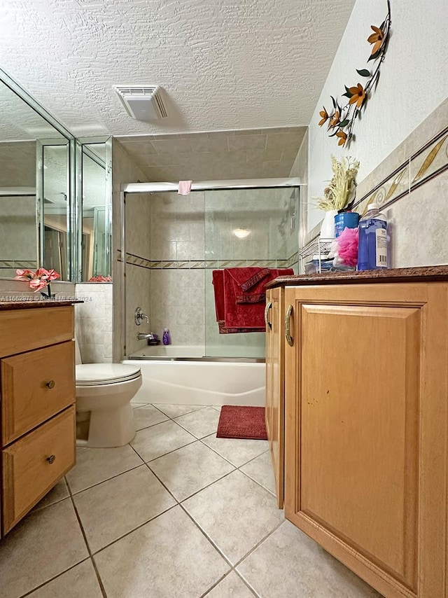 full bathroom with vanity, a textured ceiling, tile patterned flooring, shower / bath combination with glass door, and toilet