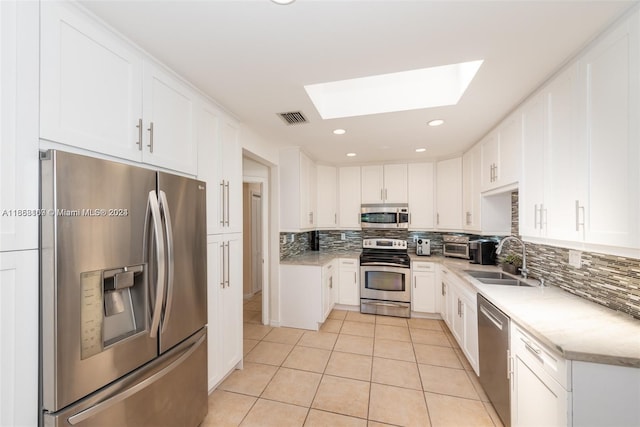 kitchen with stainless steel appliances, white cabinets, a skylight, and tasteful backsplash