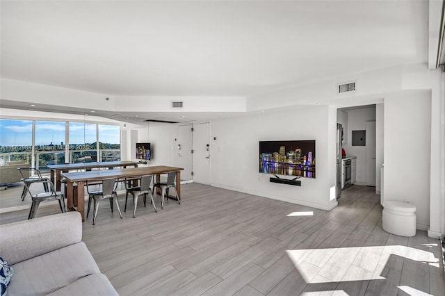 living room featuring light wood finished floors, electric panel, visible vents, and baseboards