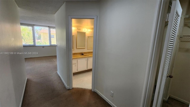 hallway featuring dark carpet, a textured ceiling, and sink