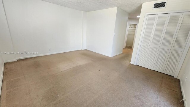 unfurnished bedroom with a textured ceiling, light colored carpet, and a closet