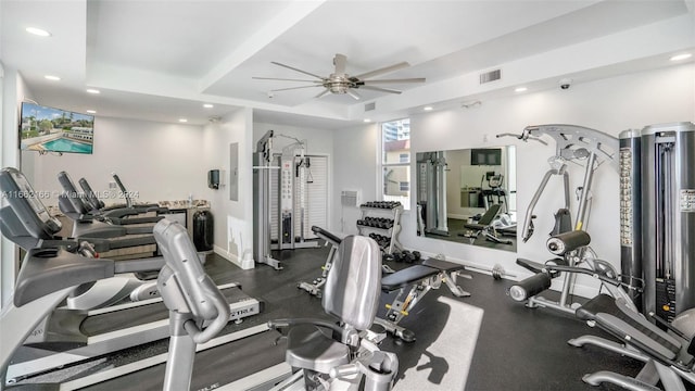 gym with a tray ceiling and ceiling fan