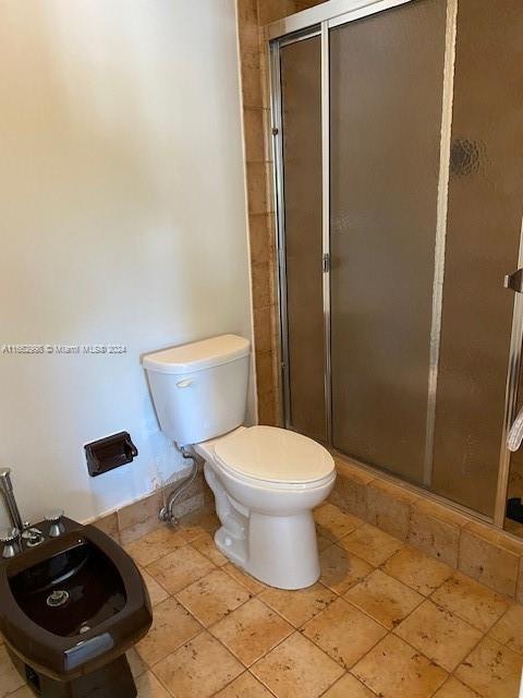 bathroom featuring toilet, tile patterned floors, and a shower with shower door