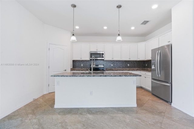 kitchen with tasteful backsplash, an island with sink, white cabinets, appliances with stainless steel finishes, and decorative light fixtures