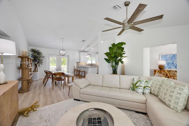 living room featuring ceiling fan with notable chandelier, light wood-type flooring, and vaulted ceiling