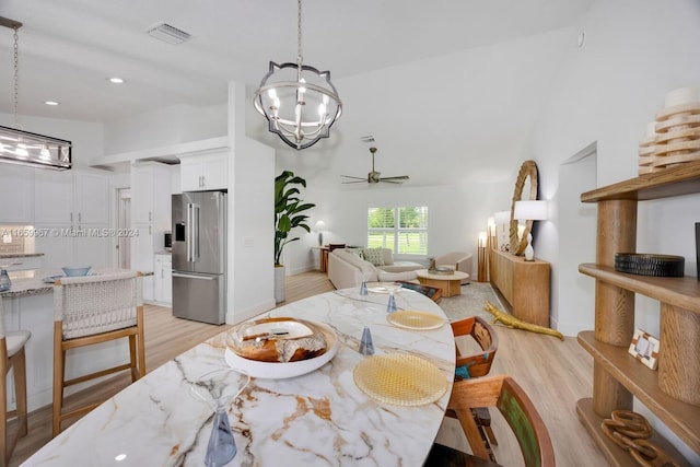 dining area with light wood-type flooring, ceiling fan with notable chandelier, and high vaulted ceiling