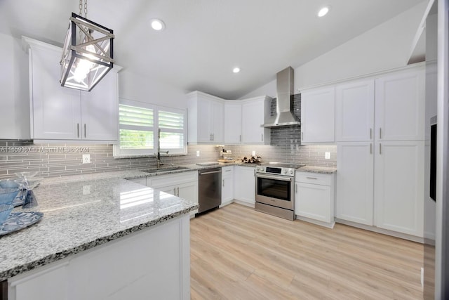 kitchen with lofted ceiling, hanging light fixtures, wall chimney exhaust hood, white cabinetry, and appliances with stainless steel finishes