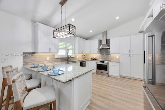 kitchen featuring hanging light fixtures, wall chimney exhaust hood, white cabinetry, stainless steel appliances, and vaulted ceiling